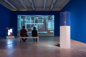 It’s in the Game. 2017. 16:32. 1-channel video (loop, color, sound) with 2 monitors in vitrines on pedestals, Rosco Chroma Key blue paint, orange extension cords. Image courtesy the artist and Bridget Donahue Gallery. © the artist. Photo Credit: Constance Mensh.